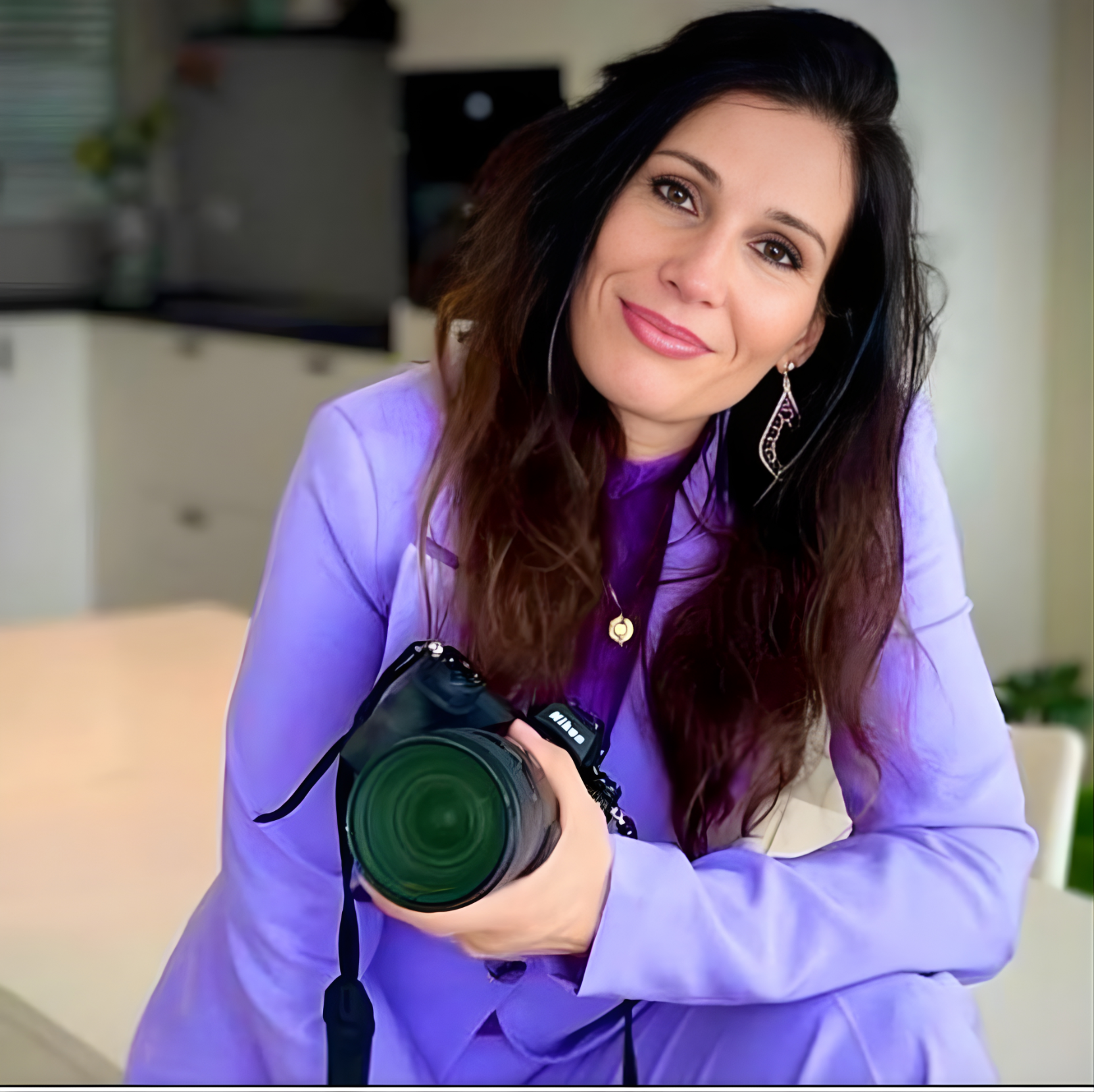 A woman in a purple suit holds a camera, ready to capture a moment with a focused expression.